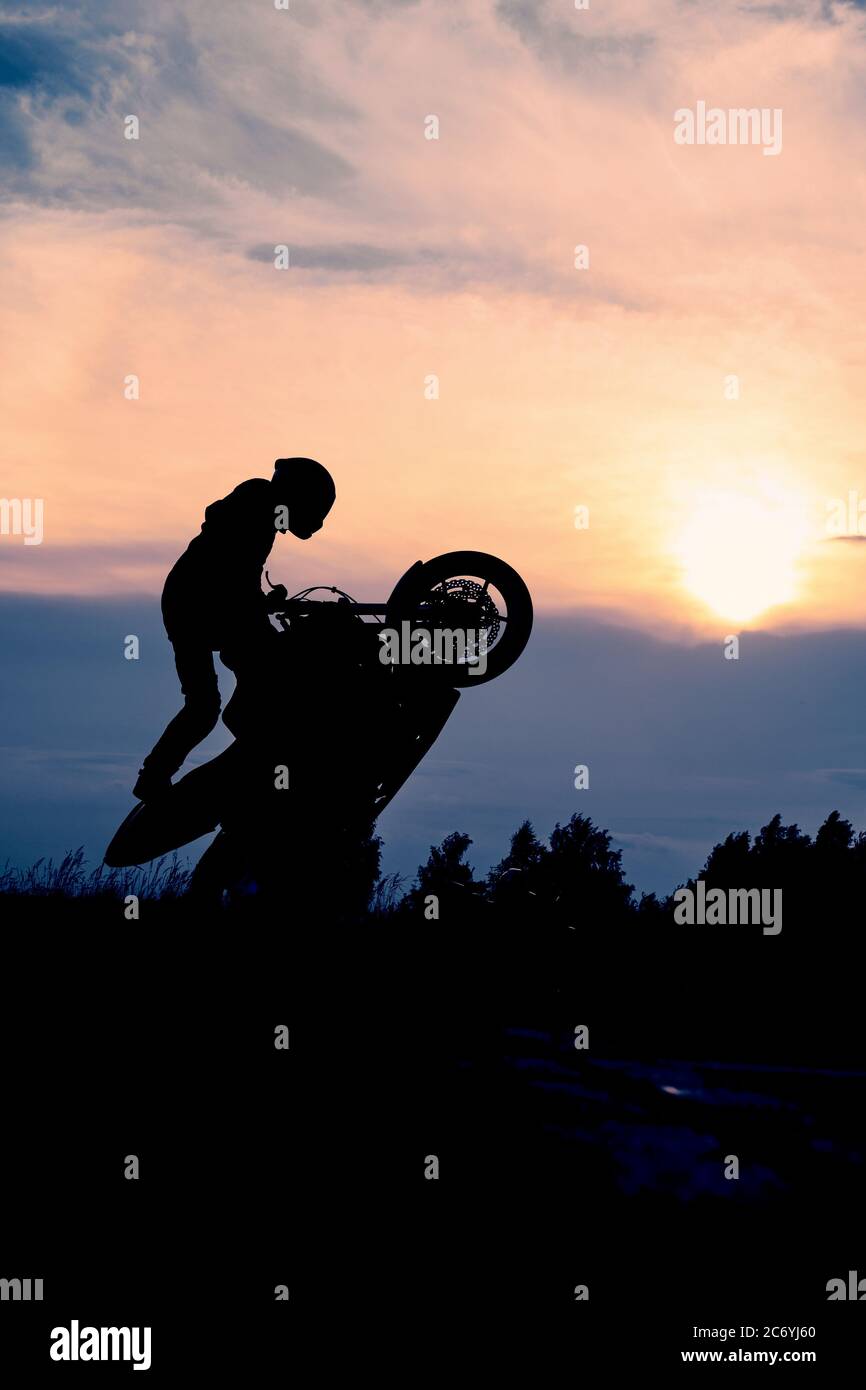 La silhouette di un motociclista al tramonto. Moto rider che fa una acrobazie sulla sua moto. Foto Stock