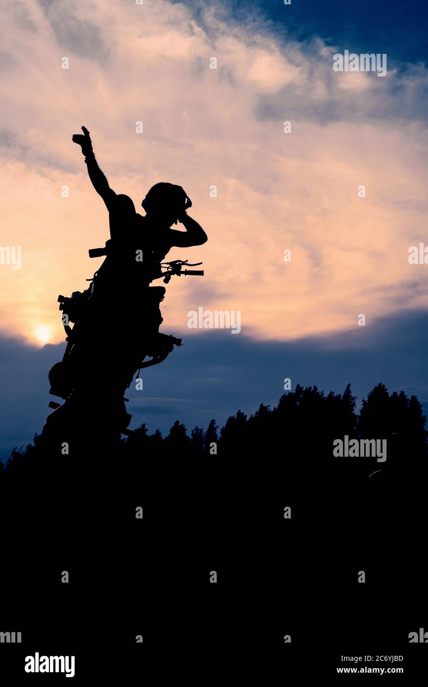 La silhouette di un motociclista al tramonto. Moto rider che fa una acrobazie sulla sua moto. Foto Stock