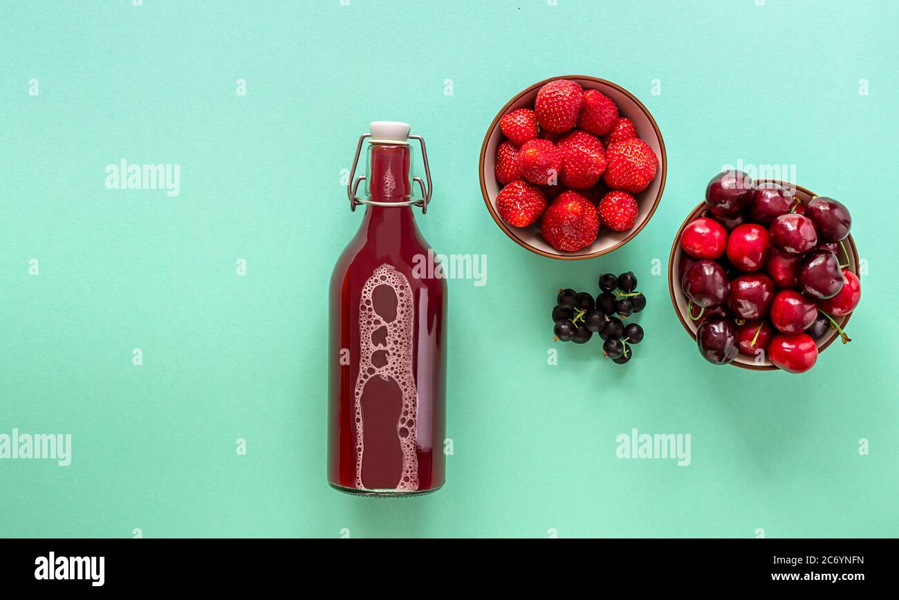 Succo di frutti di bosco fresco in bottiglia di vetro con fragola matura, ciliegia e ribes nero Foto Stock
