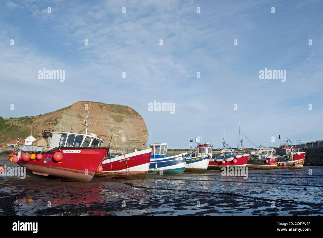 Barche a bassa marea nel porto di Staithes con Cowbar Nab sullo sfondo Foto Stock