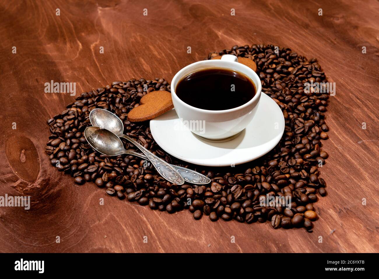 White tazza da caffè, a forma di cuore e di panpepato due cucchiai su un cuore base sagomata realizzata da chicchi di caffè - immagine Foto Stock