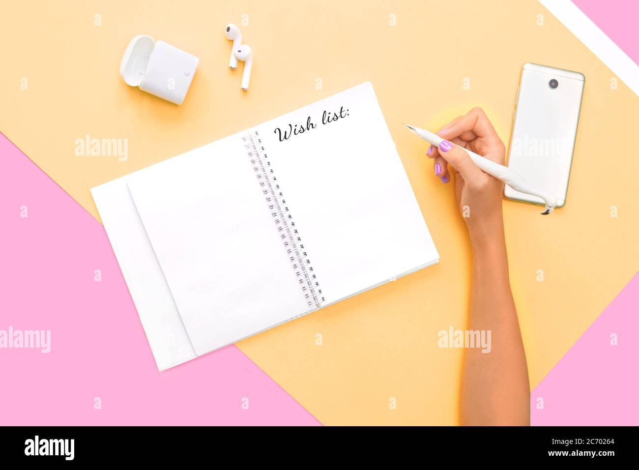 Scritta wishlist in nota, concetto blogger. Vista dall'alto di cuffie, telefono e notebook con mano e una perfetta manicure luminosa sullo sfondo rosa arancione Foto Stock