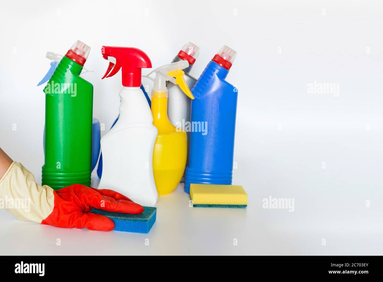 Mano con spugna e bottiglie in plastica con prodotti chimici per la pulizia domestica Foto Stock