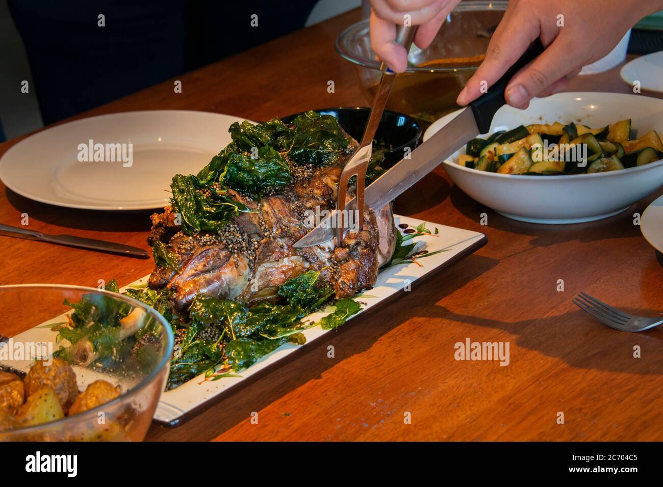 Affettare una succosa gamba di agnello (cucinata sous vide) su un piatto. Mani che tengono forchetta e coltello e agnello decorato con menta e semi di senape. Foto Stock