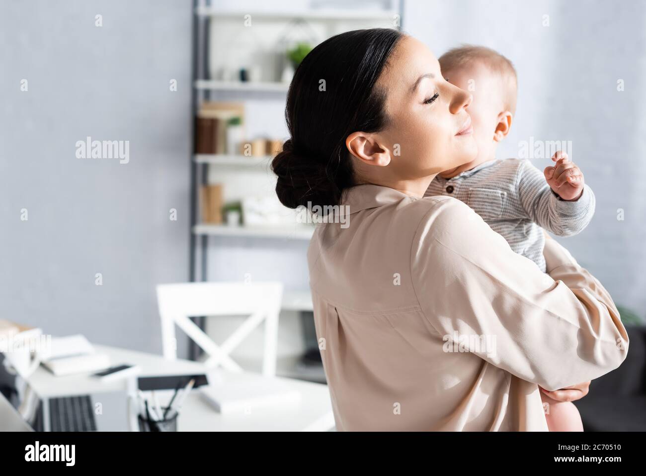 attraente madre che tiene in armi e abbracciando cute figlio del bambino in romper del bambino Foto Stock