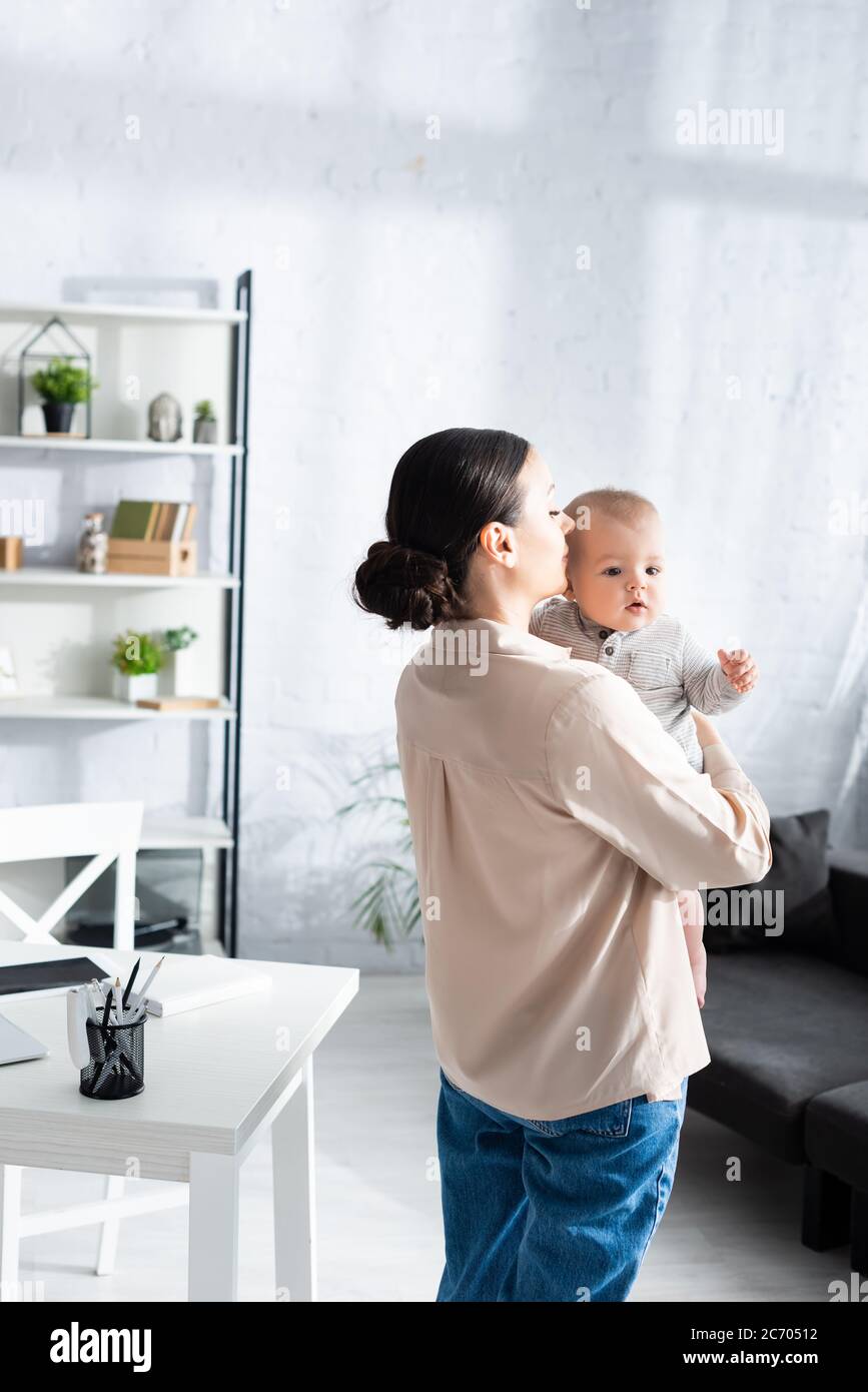 attraente madre in piedi e tenendo in braccio cute figlio del bambino nel romper del bambino Foto Stock