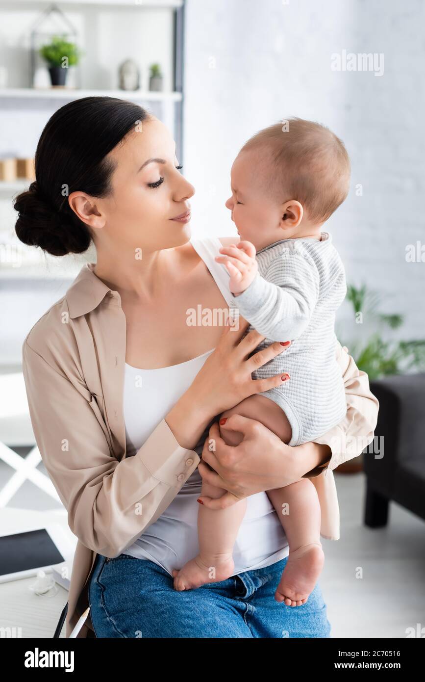 attraente madre che tiene in armi e guardando il figlio carino del bambino nel romper del bambino Foto Stock