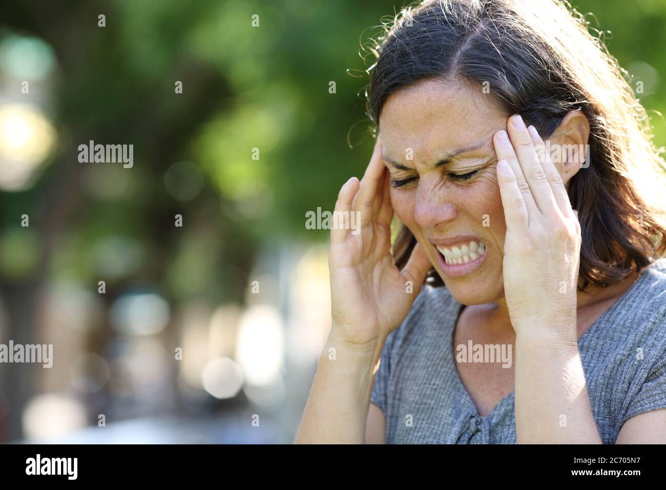 Donna adulta in dolore che soffre di emicrania in piedi nel parco in estate Foto Stock