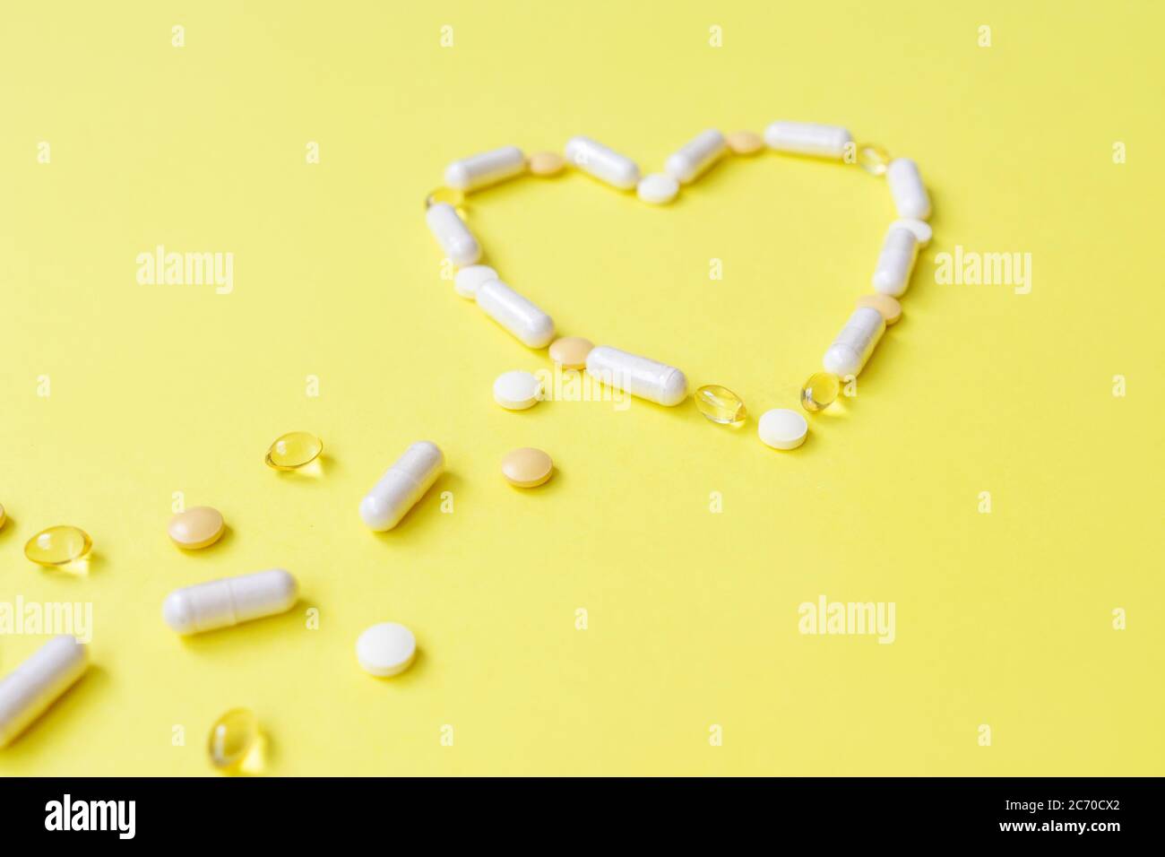 Le vitamine volano e fanno il cuore sul giallo. Vista frontale. Foto Stock