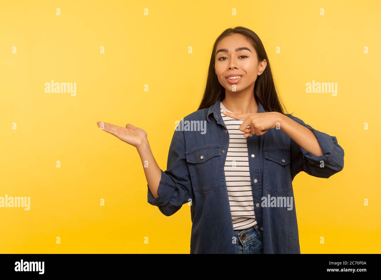 Attenzione, pubblicità piacevole del prodotto! Ritratto di ragazza felice in camicia di denim tenendo spazio di copia con il palmo, che punta a vuoto luogo per immagine commerciale. i Foto Stock