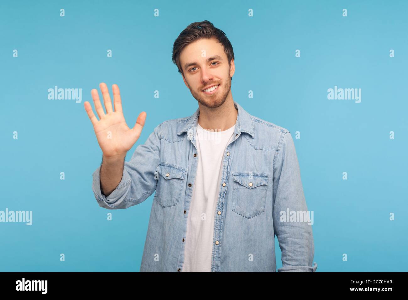 Ciao! Ritratto di amico sorridente bell'uomo in camicia di jeans operaio alzando mano, accogliente con ciao gesto, saluto e incontro con e ospitale Foto Stock