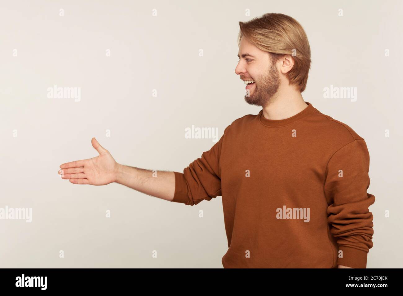 Vista laterale di positivo amichevole ospitale uomo bearded in felpa in piedi con mano estensibile, offrendo handshake al partner, saluto sul lavoro in Foto Stock