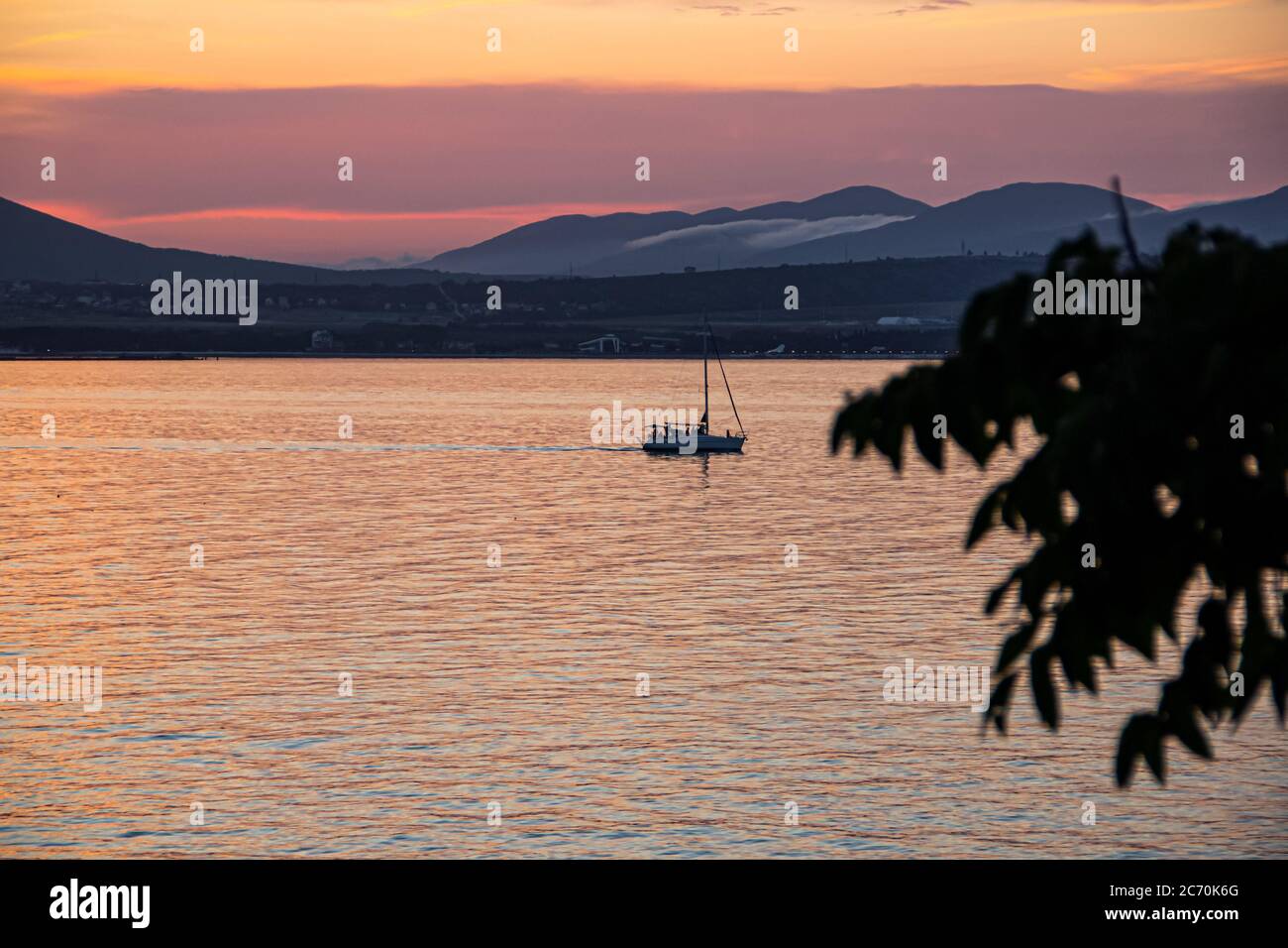 Luminoso arancio al tramonto, uno yacht da diporto sullo sfondo delle montagne della città di Gelendzhik. Costa del Mar Nero Foto Stock