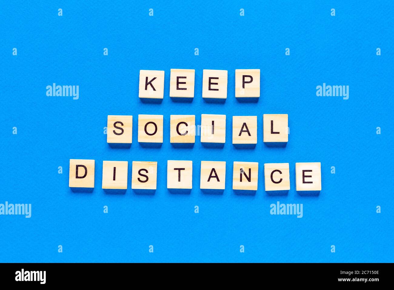 Le parole mantengono la distanza sociale. Iscrizione in legno su sfondo blu. Segno di informazione di mantenere la distanza sociale da blocchi su sfondo blu. Top vi Foto Stock