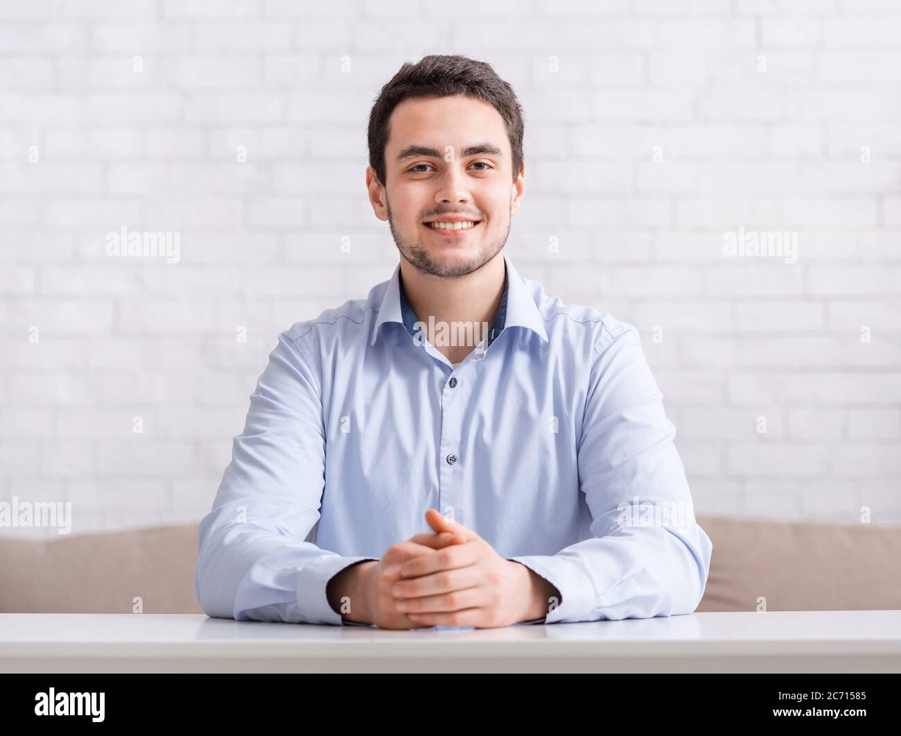 Riunioni online e lavoro da casa. Ragazzo sorridente e amichevole in camicia con le mani sul tavolo Foto Stock