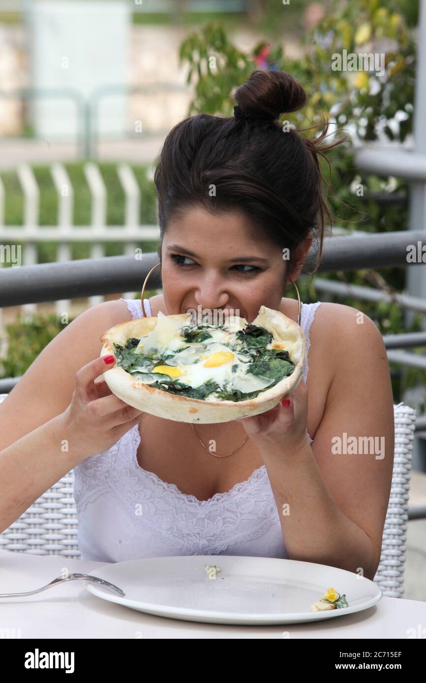 La giovane donna mangia una pizza con spinaci e uova Foto Stock