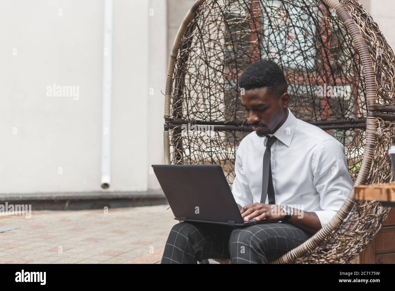 Uomo d'affari africano che lavora su un computer portatile in un caffè all'aperto seduto sulla sedia a uova Foto Stock