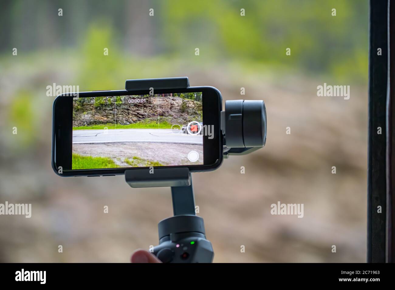 Smartphone con stabilizzatore che guarda video di una strada di montagna. Foto Stock