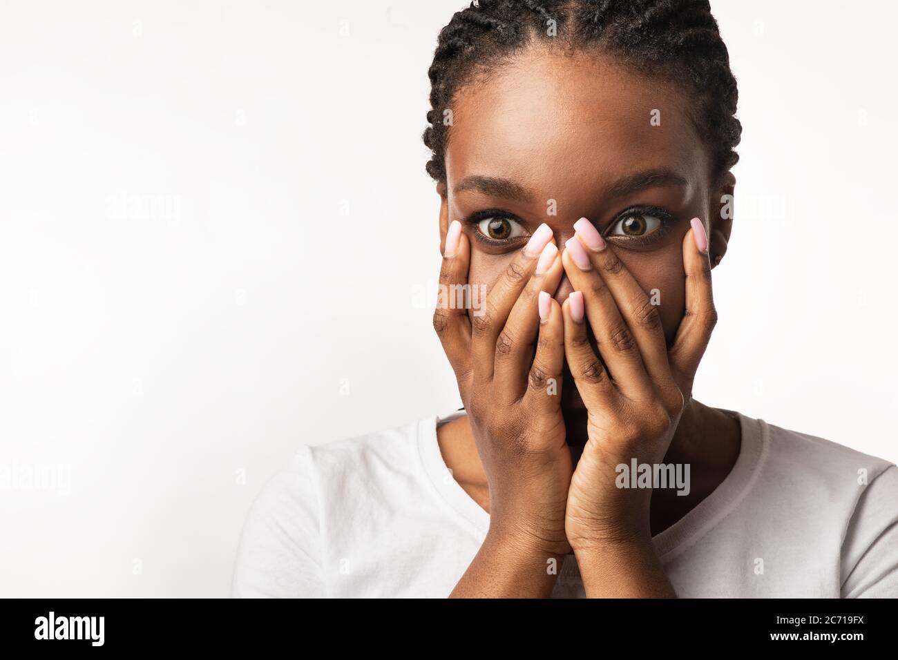 Ragazza africana scioccata guardando la fotocamera che copre la bocca, sfondo bianco Foto Stock
