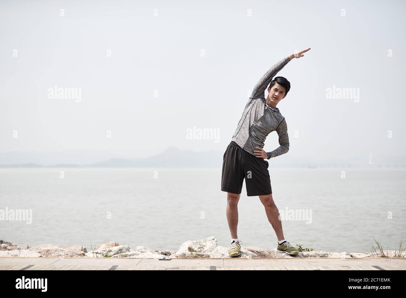 giovane uomo adulto asiatico che allunga il corpo all'aperto vicino al mare Foto Stock