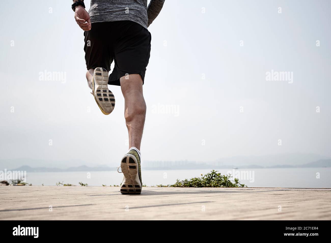 primo piano delle gambe di un corridore asiatico che corre sul mare, vista posteriore Foto Stock