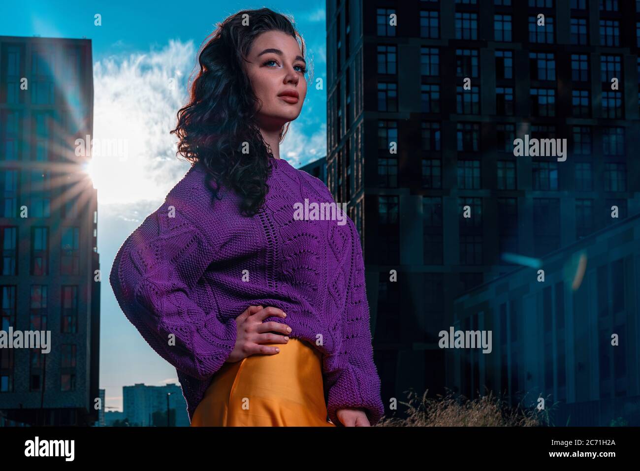 Bella donna Brunette che indossa una maglia viola brillante in lana o cotone pullover. Paesaggio urbano moderno. Felpa a maglia e filato Luxury fatti a mano Foto Stock