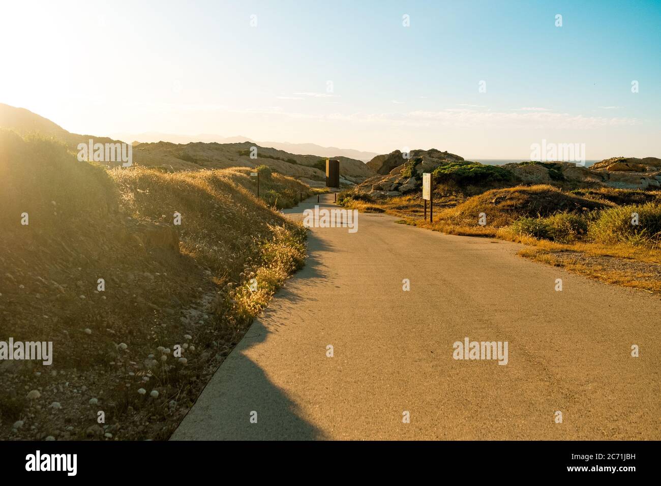 vuota strada rocciosa e curvilinea tra vergine, selvaggio paesaggio al tramonto, un sentiero e simbolo e vita, scelte e crescita Foto Stock