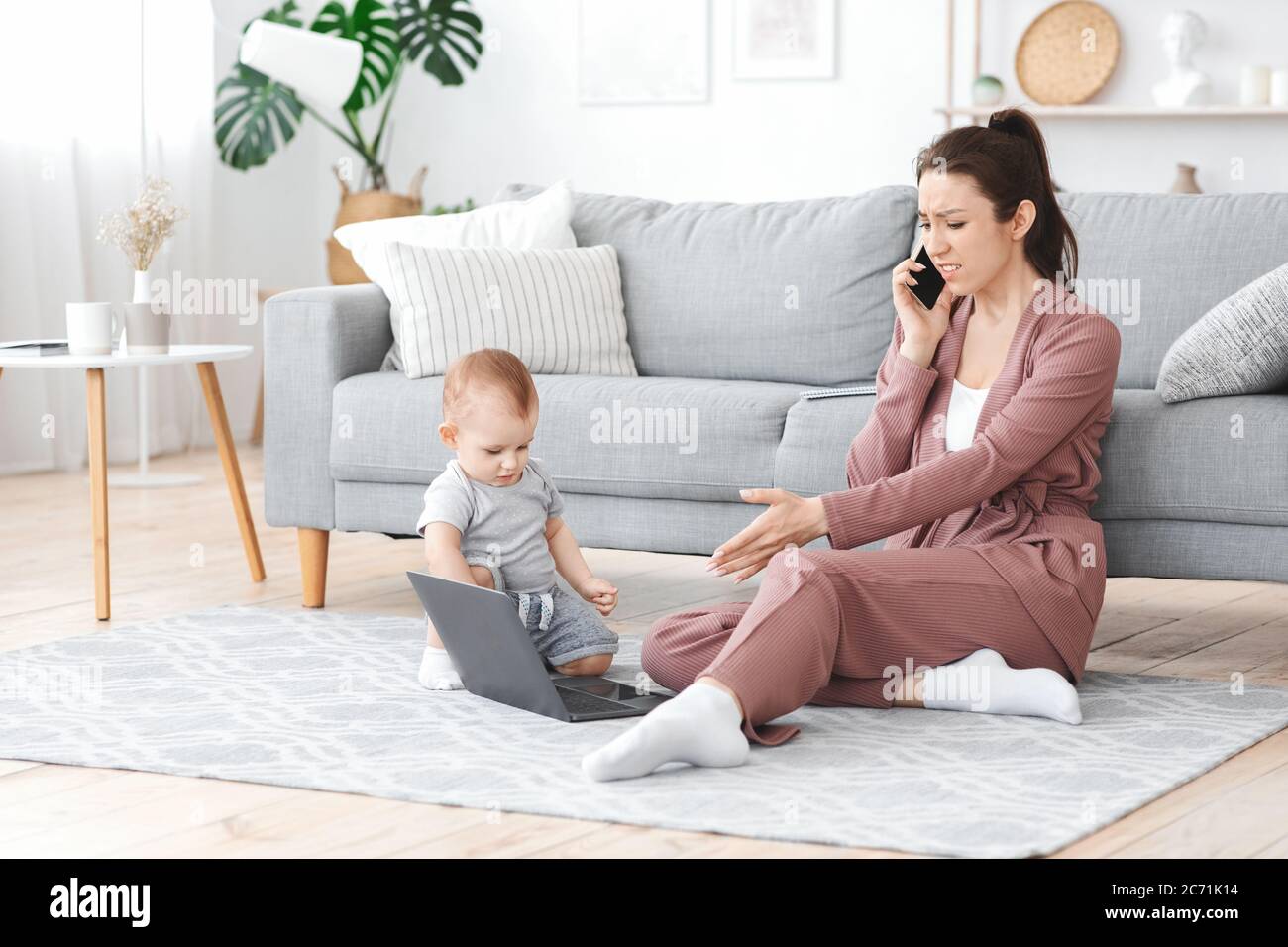 Infastidita donna che parla su Cellphone mentre il suo bambino tocca il portatile della mamma Foto Stock