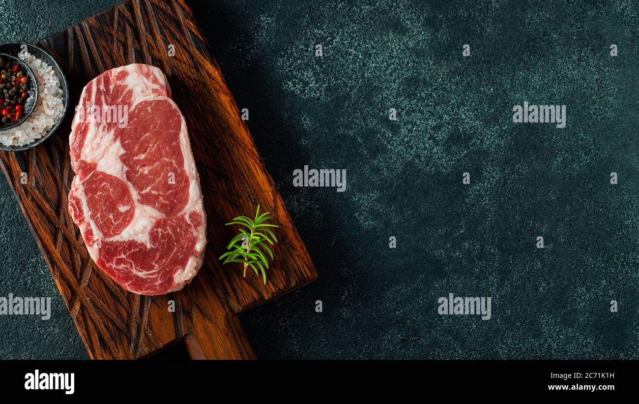 Carne fresca cruda Ribeye Steak e stagionatura su fondo scuro. Vista dall'alto con spazio per la copia. Disposizione piatta Foto Stock