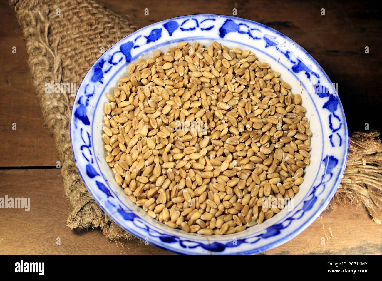 Pila di grano integrale organico. Grano fresco raccolto in una ciotola isolata su sfondo di legno. Grani di grano e farina di grano. Foto Stock