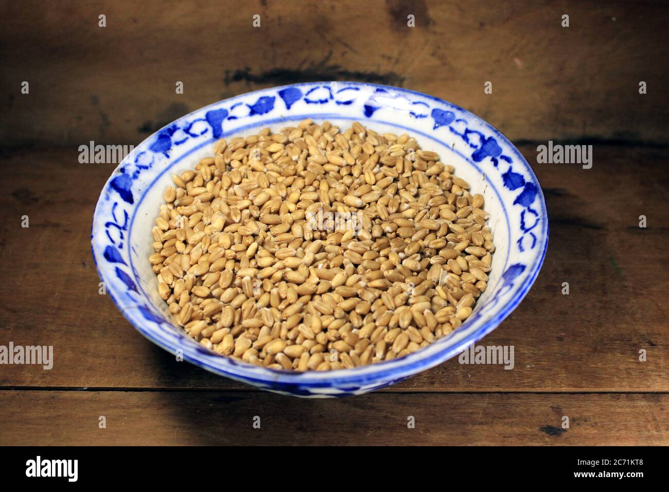 Pila di grano integrale organico. Grano fresco raccolto in una ciotola isolata su sfondo di legno. Grani di grano e farina di grano. Foto Stock