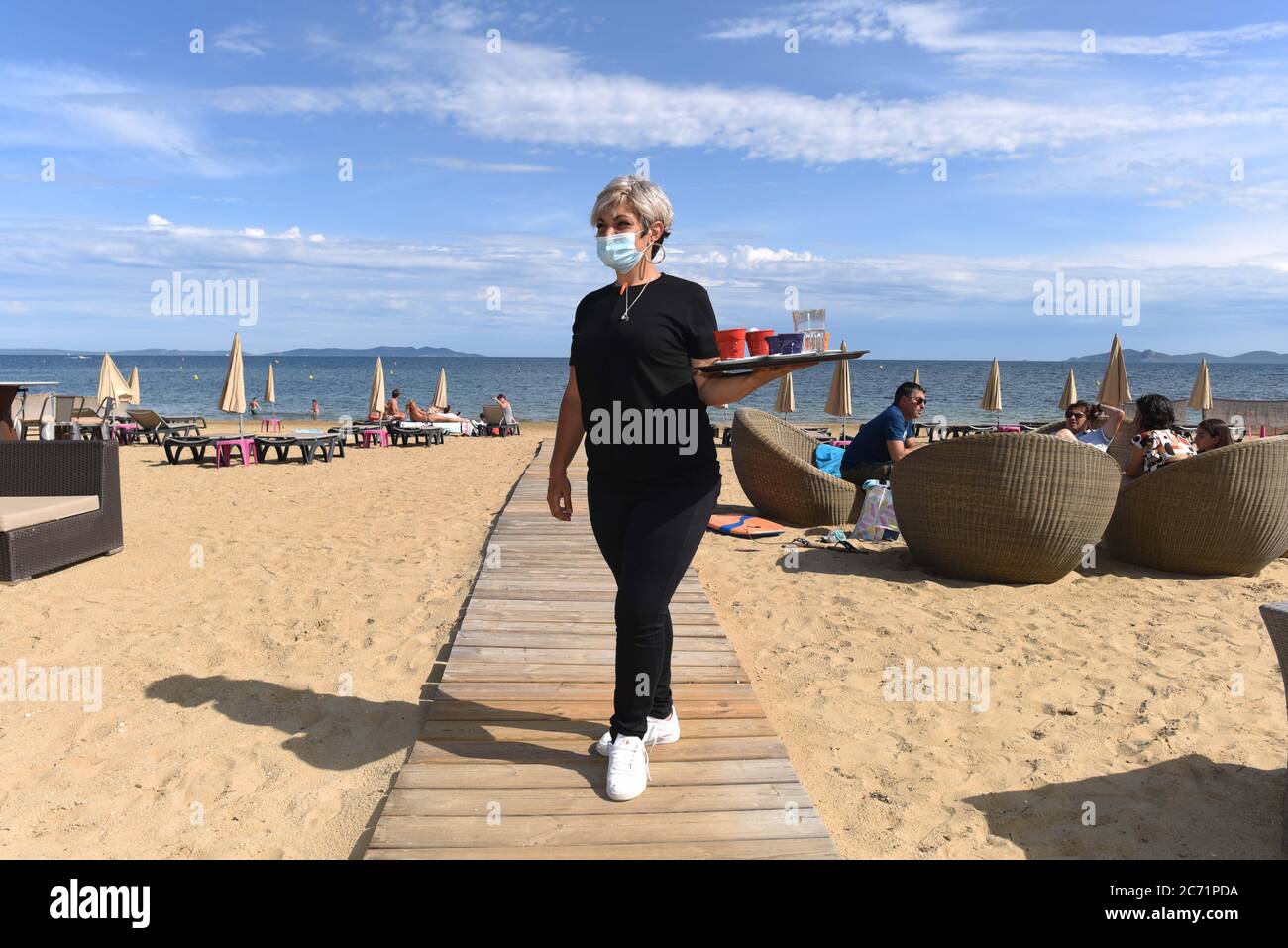 *** RIGOROSAMENTE NESSUNA VENDITA AI MEDIA O AGLI EDITORI FRANCESI - DIRITTI RISERVATI ***07 giugno 2020 - la-Londe-les-Maures, Francia: Cynthia, cameriera di la Voile Plage, porta bevande ai clienti seduti su sdraio in spiaggia. Deve indossare un facemask contro covid-19. La maggior parte delle spiagge sono state riaperte mentre le autorità francesi gradualmente facilitano il blocco del coronavirus. Foto Stock