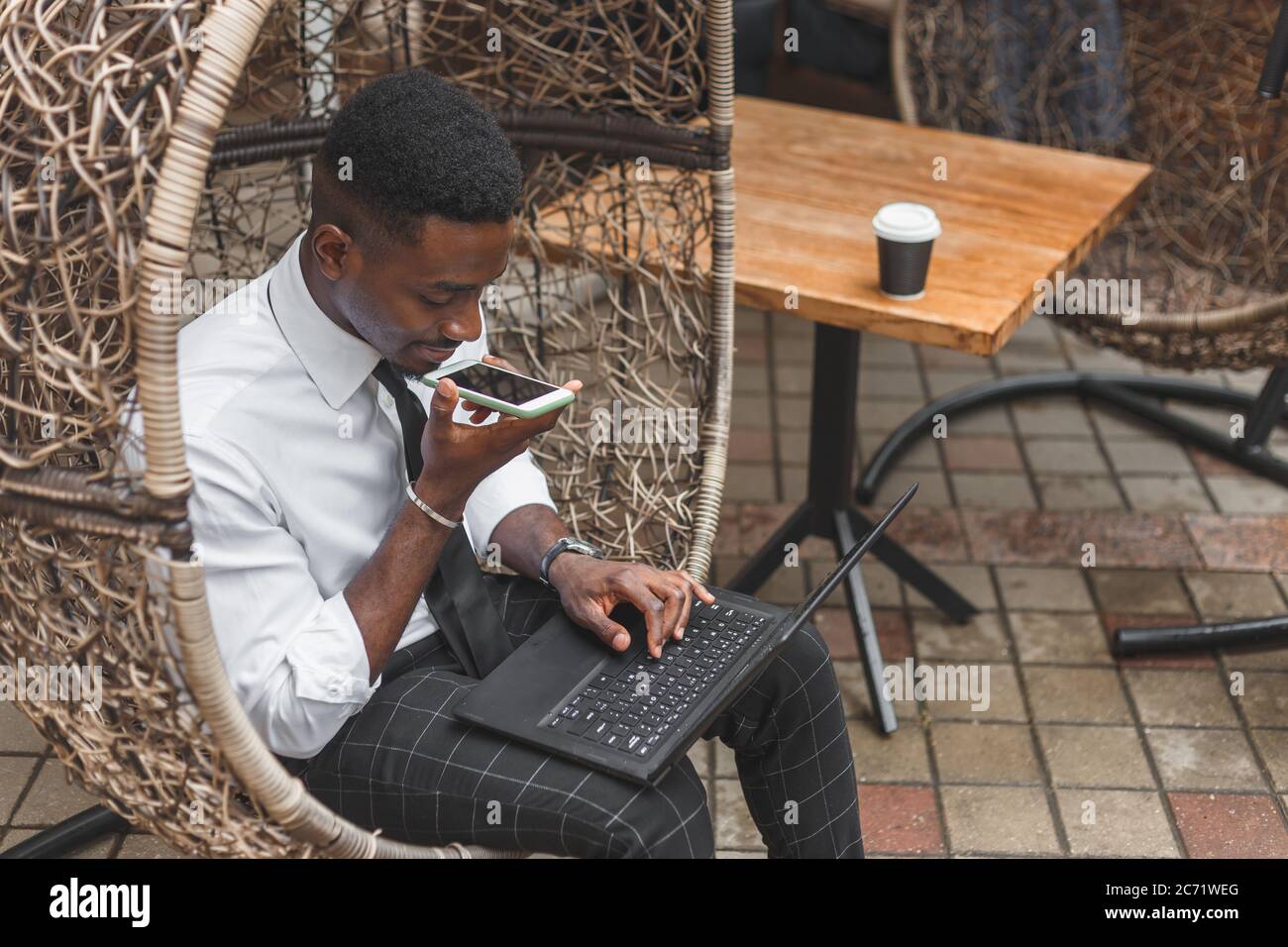 Uomo afro-americano aziendale che tiene smartphone, dettare messaggi vocali, registrare audio, utilizzando il microfono vocale. La gente lavora all'aperto Foto Stock