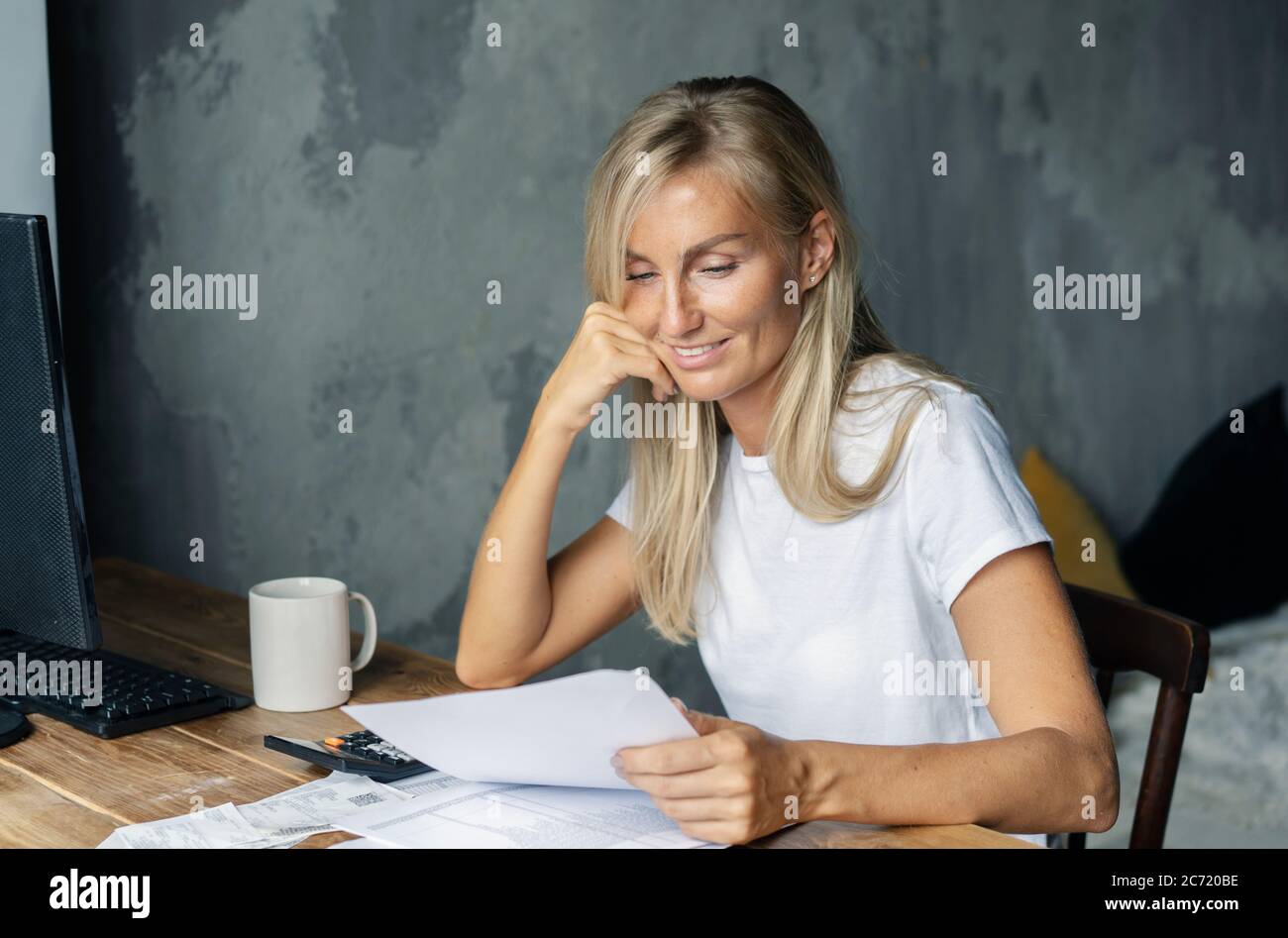 Donna al tavolo legge un documento e sorride Foto Stock