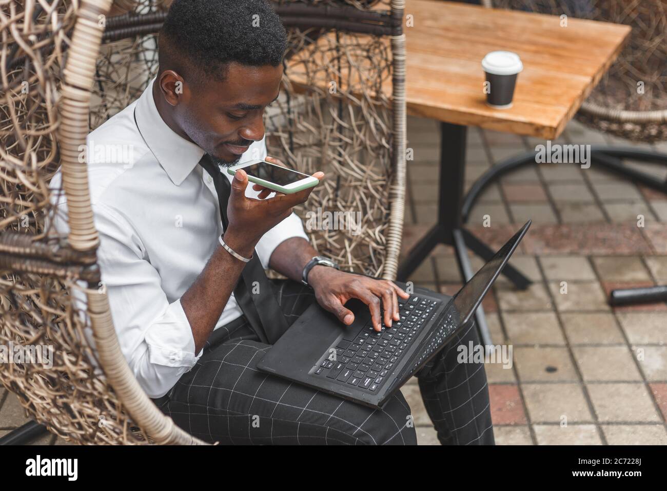 Uomo afro-americano aziendale che tiene smartphone, dettare messaggi vocali, registrare audio, utilizzando il microfono vocale. La gente lavora all'aperto Foto Stock