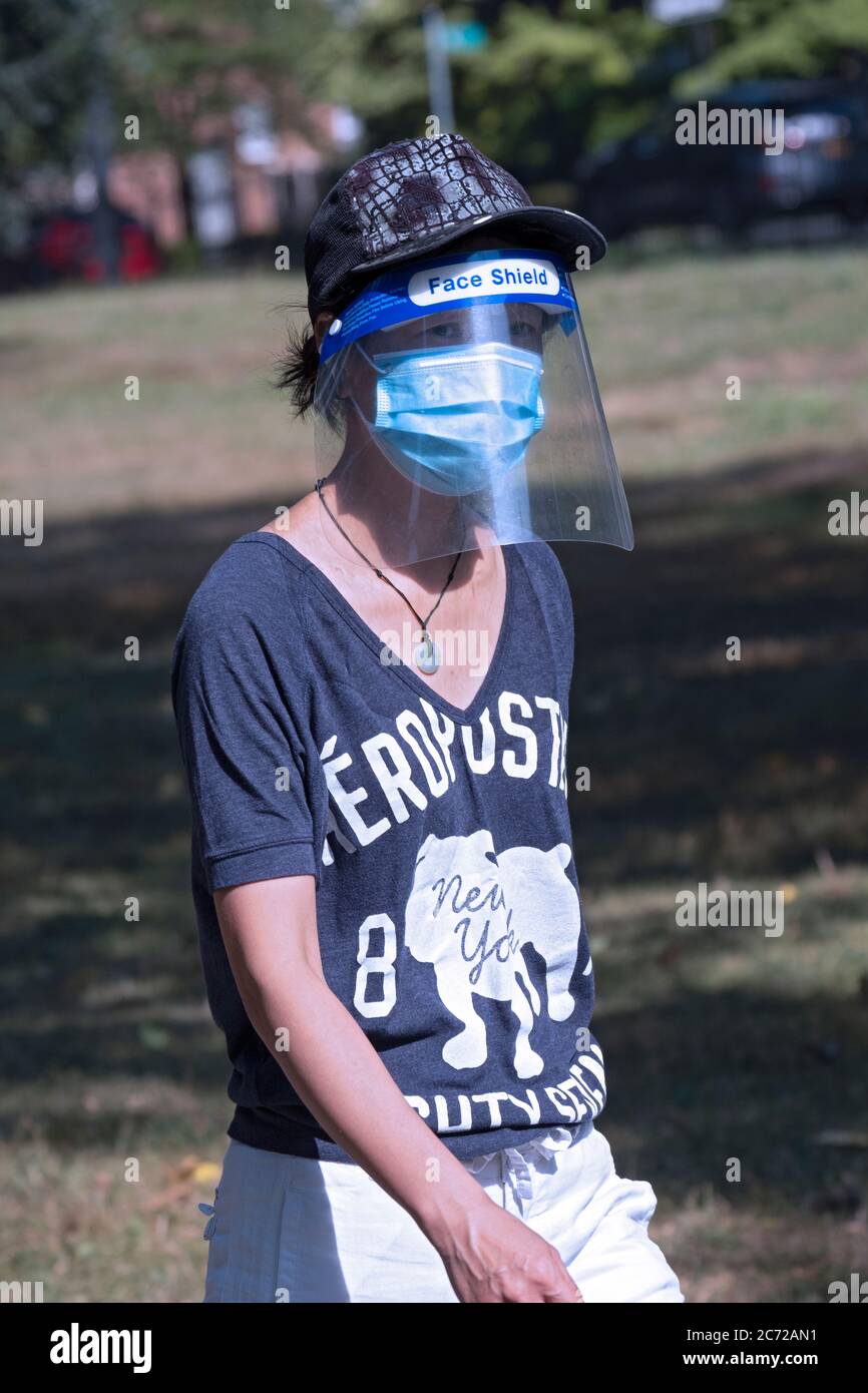 Una snella donna asiatica americana fuori per una camminata di esercitazione che indossa sia una maschera chirurgica che uno schermo facciale. A Flushing, Queens, New York City. Foto Stock