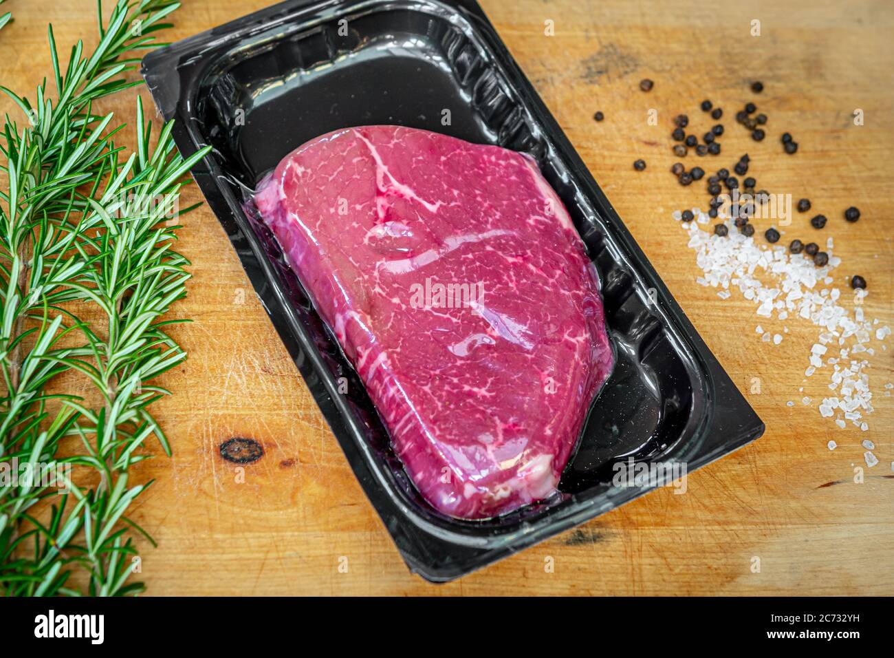 Bistecca di manzo in confezionamento sottovuoto e spezie su tagliere di legno Foto Stock