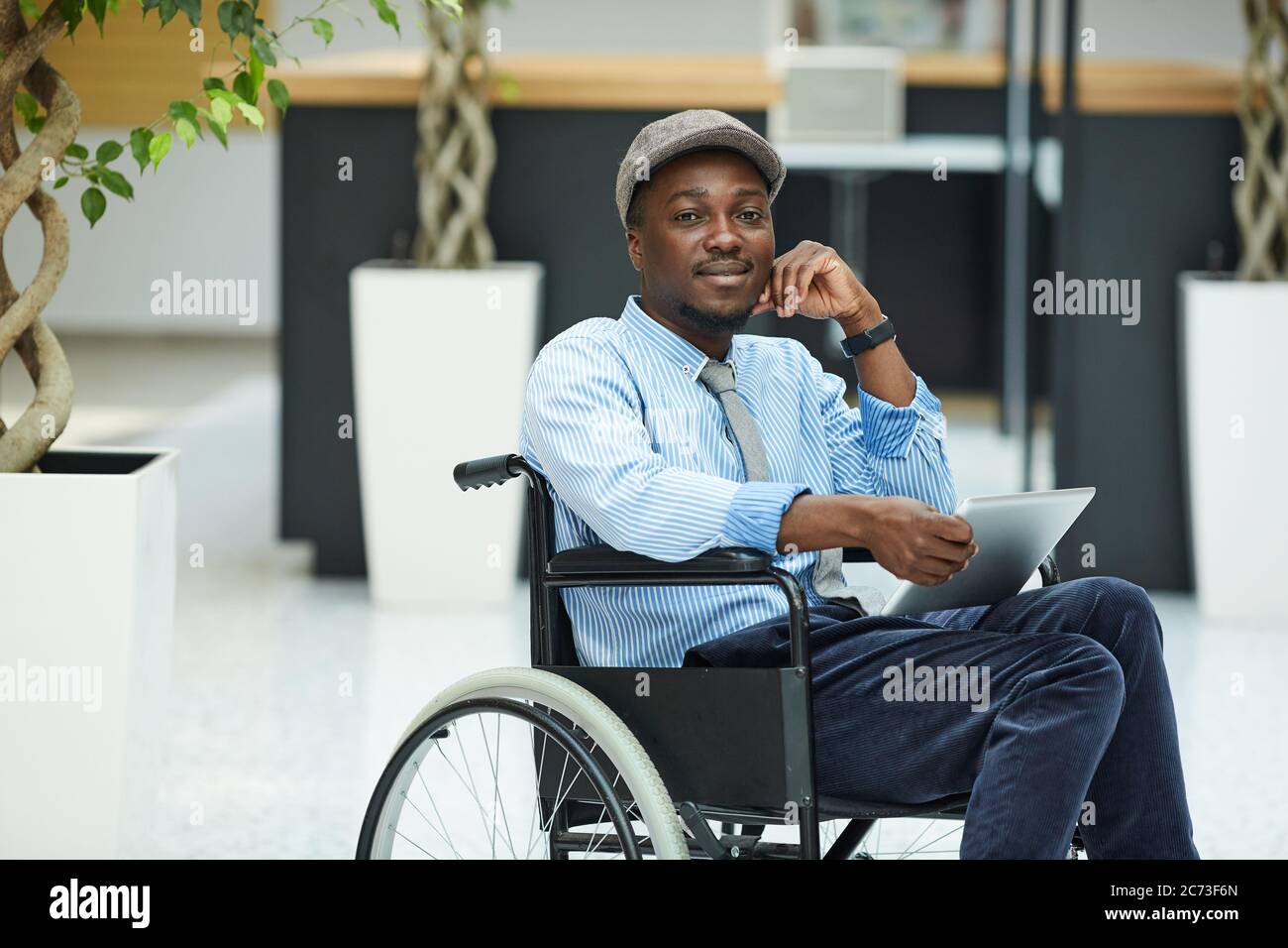 Ritratto di un uomo africano disabile seduto in sedia a rotelle e utilizzando un tablet digitale Foto Stock