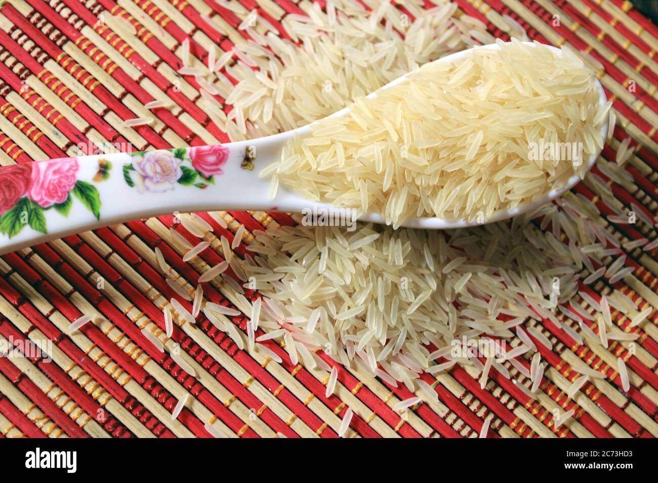 Grani di riso in un cucchiaio di plastica bianca su sfondo multicolore. Macro sfondo di riso bianco. Riso Basmati su un palo isolato su sfondo modello. Foto Stock