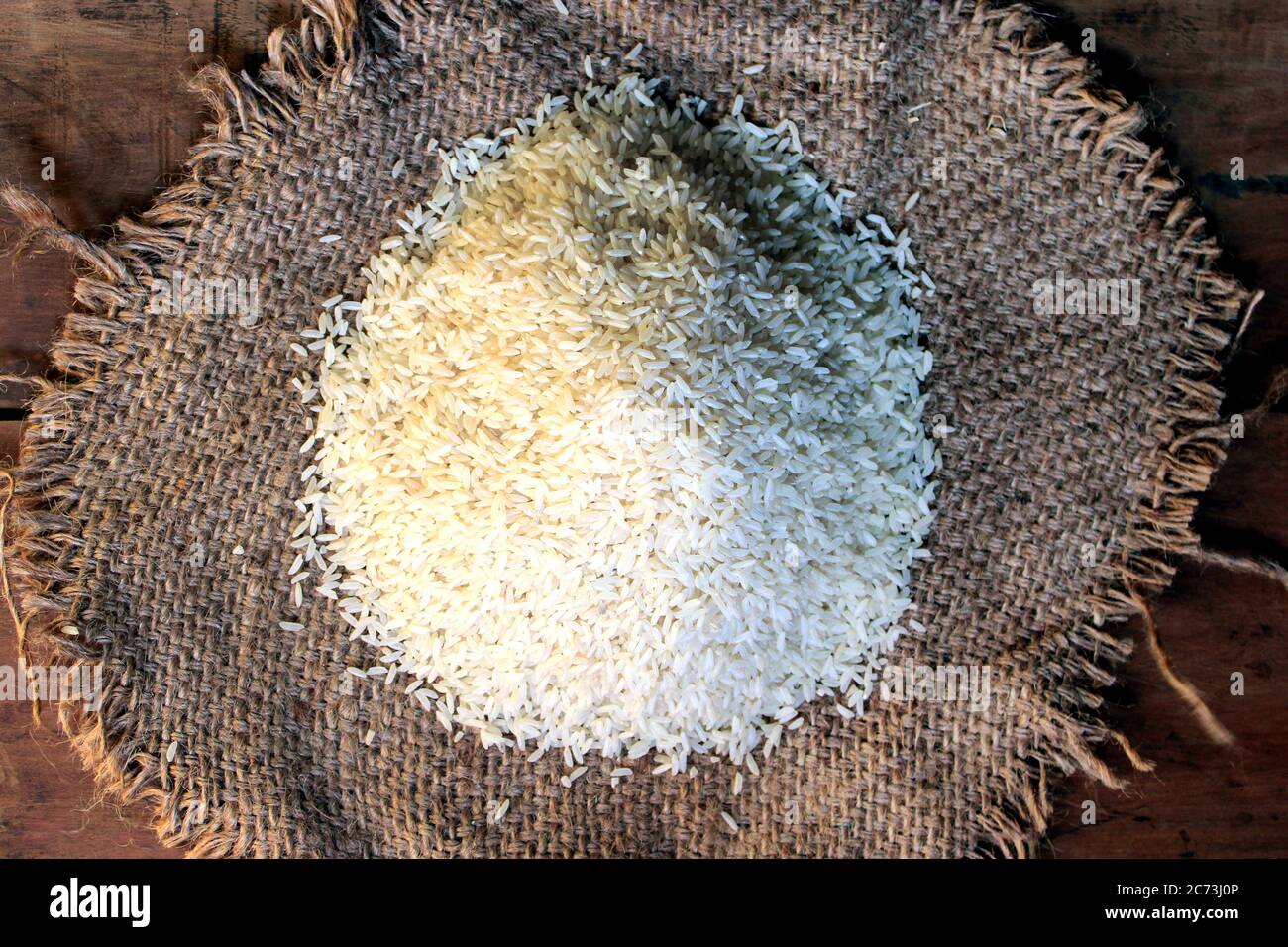 Riso fuori da piccolo sacco isolato su sfondo di legno. Riso fresco in sacco su fondo testurizzato di legno. Chiudi su grano di riso crudo su panno di sacco. Foto Stock