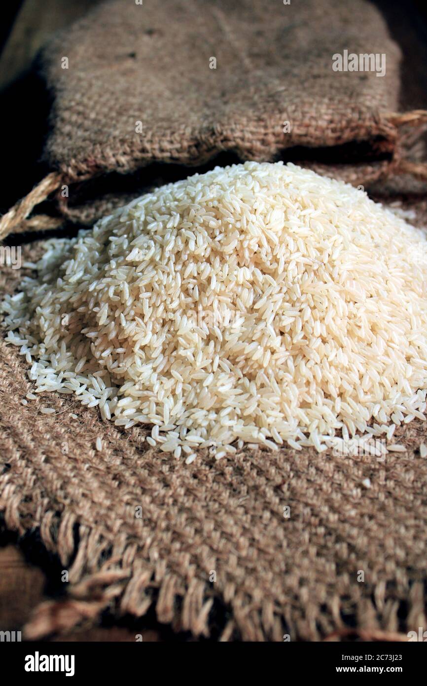Riso fuori da piccolo sacco isolato su sfondo di legno. Riso fresco in sacco su fondo testurizzato di legno. Chiudi su grano di riso crudo su panno di sacco. Foto Stock