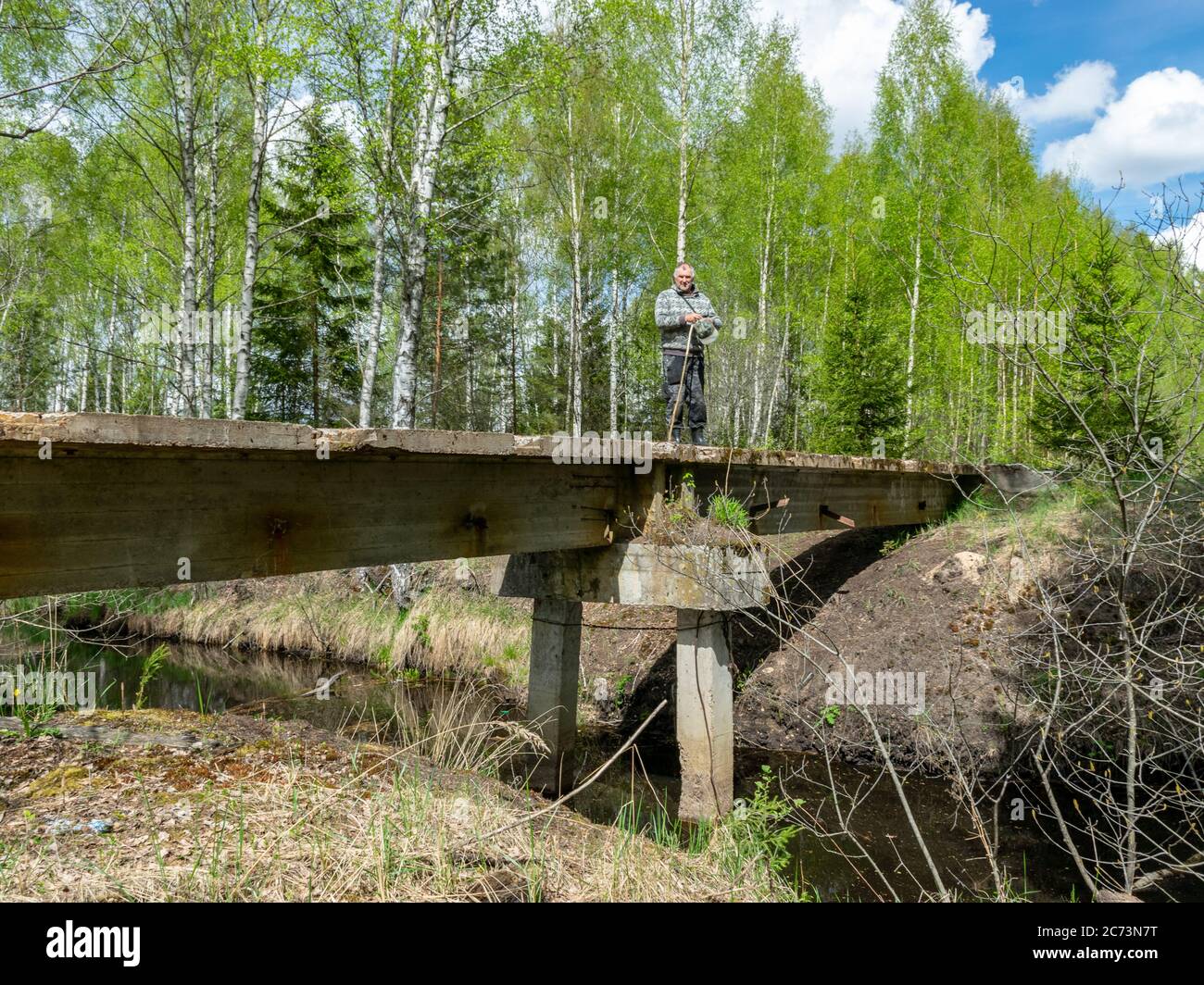 paesaggio con un uomo su un vecchio e abbandonato ponte di cemento armato per un treno, un ponte su una fossa paludoso, un treno torba camminato sul ponte Foto Stock
