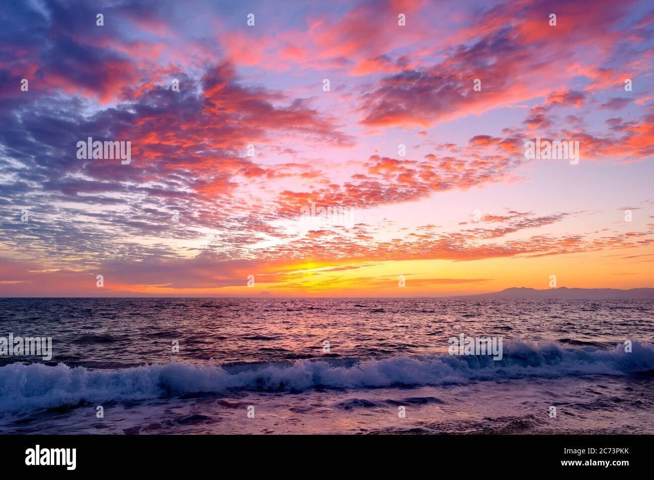 Un colorato Ocean Sunset Sky mentre un'onda dolce rotola a Shore Foto Stock