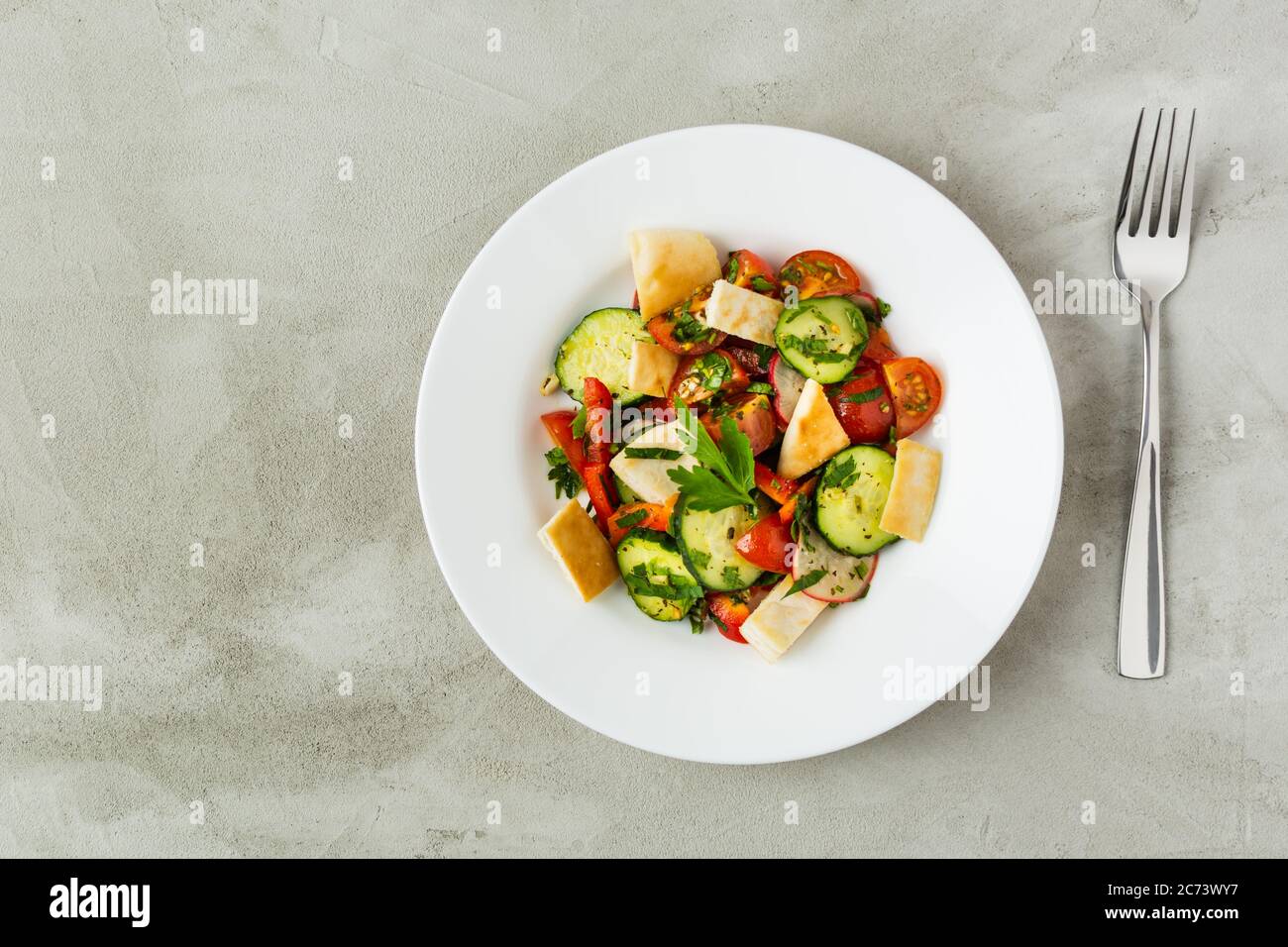 Su sfondo grigio in un piatto bianco insalata libanese Fattush. Verdure. Vegetarianismo. Disposizione piatta Foto Stock