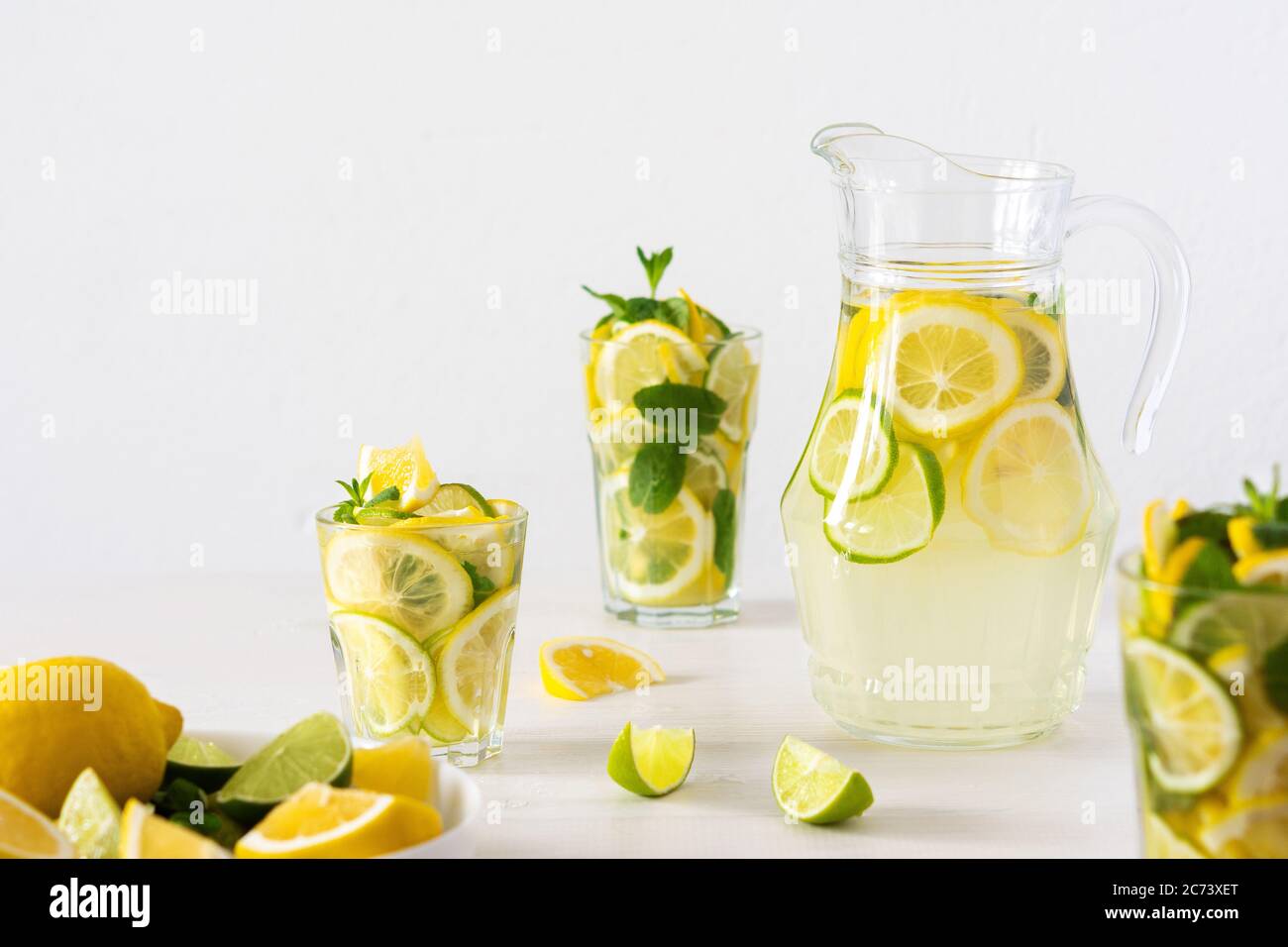 Bevanda estiva rinfrescante di limone, lime e menta, caraffa con limonata e bicchieri e fette di agrumi Foto Stock