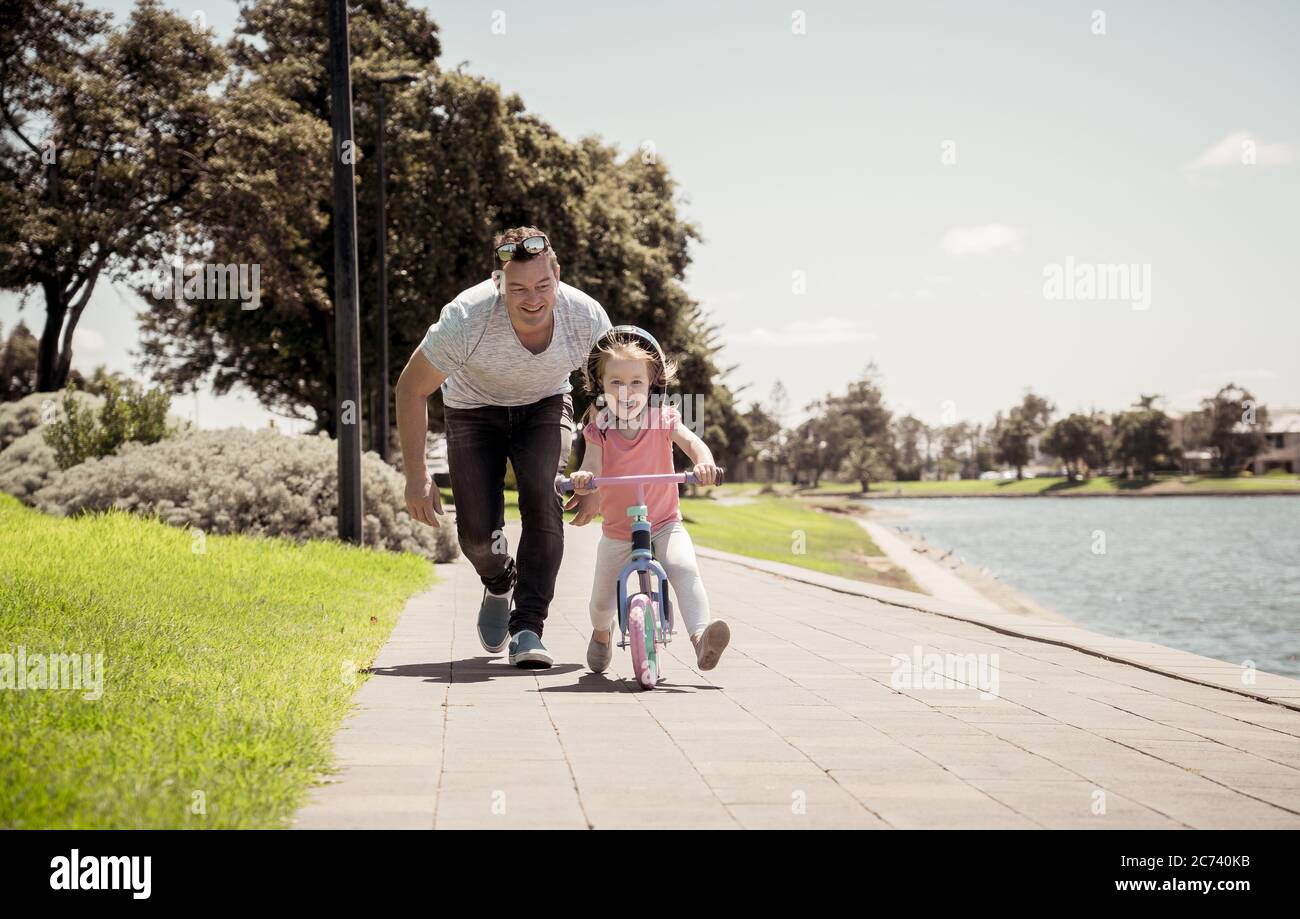 Bambina imparando a fare una bicicletta con suo padre nel parco vicino al lago. Padre e figlia si legano e si divertono insieme. Felice famiglia, fuori Foto Stock