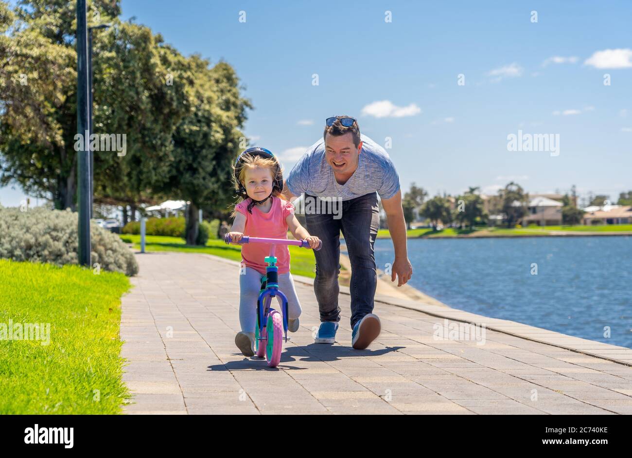 Bambina imparando a fare una bicicletta con suo padre nel parco vicino al lago. Padre e figlia si legano e si divertono insieme. Felice famiglia, fuori Foto Stock