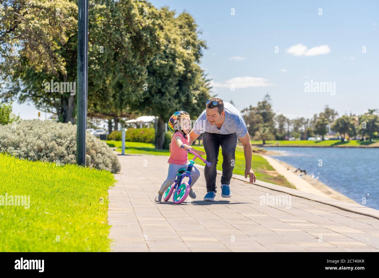 Bambina imparando a fare una bicicletta con suo padre nel parco vicino al lago. Padre e figlia si legano e si divertono insieme. Felice famiglia, fuori Foto Stock
