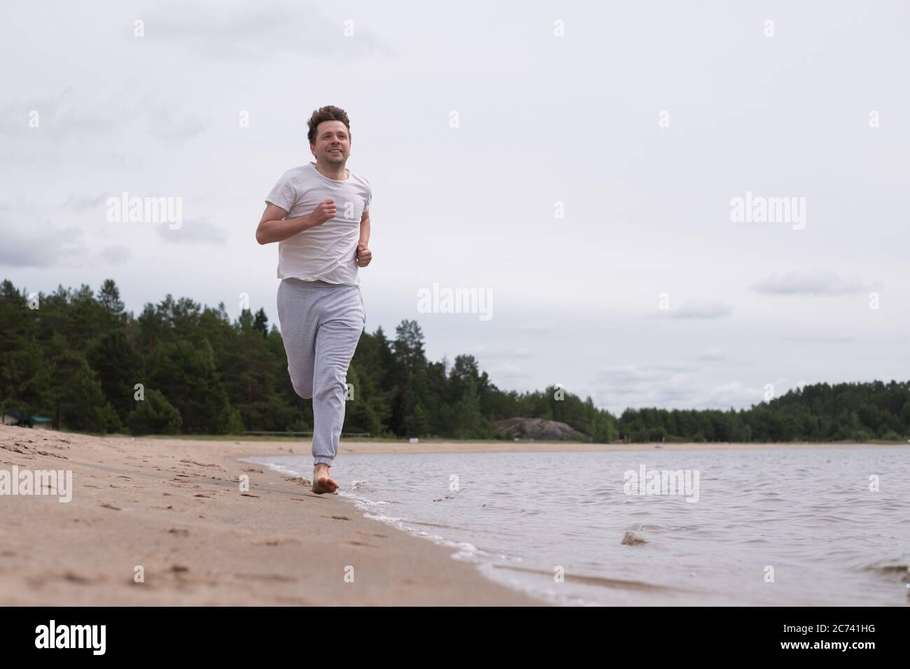 Uomo in abbigliamento fitness che corre lungo la spiaggia di sabbia Foto Stock