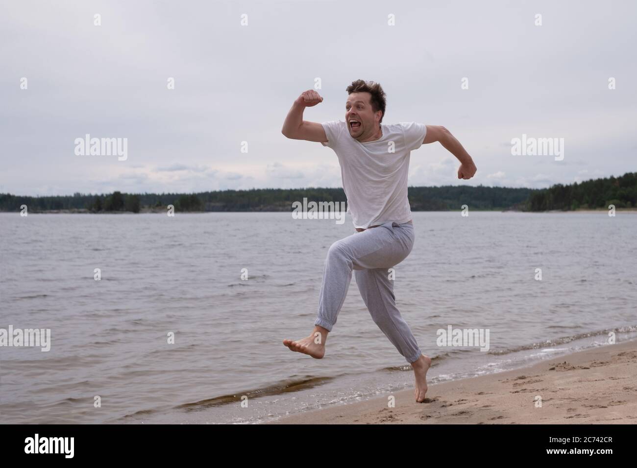 Uomo in abbigliamento fitness che corre lungo la spiaggia di sabbia Foto Stock